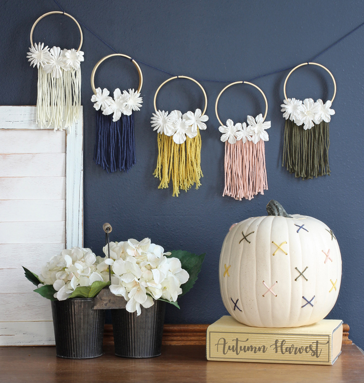 Create your own DIY fall decorations in a nontraditional color scheme: a beautiful macrame inspired mini embroidery hoop banner and a fun cross-stitched pumpkin.
